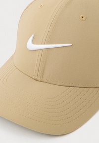 Gorra de béisbol beige de Nike con el logotipo de swoosh blanco bordado en la parte frontal, con múltiples filas de costura en el visera curvada.