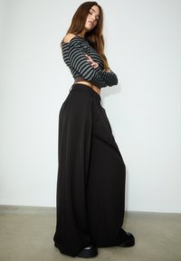Schwarze Hosen mit weitem Bein und Vorderfalten, kombiniert mit einem enganliegenden schwarz-grau gestreiften Crop-Top. Glatter Stoff, strukturiertes Design und lässige Passform.
