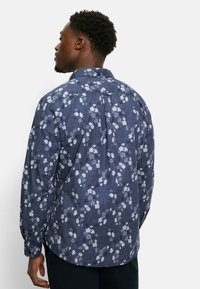 Marineblaues Hemd mit floralen Mustern in Hellblau und Weiß, langen Ärmeln, geknöpften Manschetten und einem Rückenfalten für eine entspannte Passform.