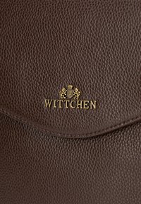 Sac à main en cuir marron avec une surface texturée, arborant un logo doré "Wittchen" et des détails en relief représentant un lion. La fermeture est de type rabat.