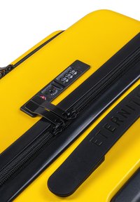 Yellow hard-shell suitcase with a black zipper, combination lock, and a textured handle. Features the word "ETERNITY" embossed on the side.