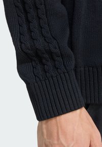 Manga de suéter de malha azul-marinho com detalhes em padrão de cabo, punho canelado, textura suave e estilo justo. Vista aproximada do braço e do tecido.