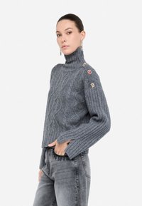 Maglione grigio a collo alto in maglia con motivo a trecce, maniche a costine e bottoni decorativi sulla spalla. Design accorciato, tessuto testurizzato.