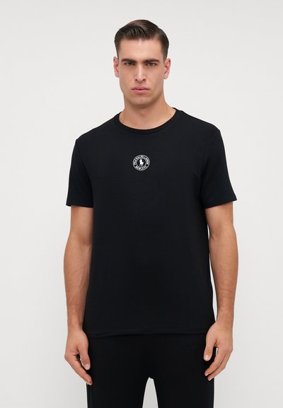 T-shirt noir à manches courtes en coton, avec un logo circulaire sur le coin supérieur gauche. Encolure ronde classique et coupe décontractée.