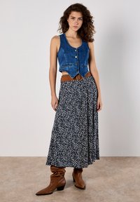 Denim vest, blue, sleeveless with buttons; paired with a flowing, navy skirt featuring a white abstract pattern; brown belted waist; brown boots.