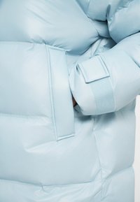 Hele sinine puhvjakott, millel on küljetasku ja velcro mansett, sujuva ja läikiva tekstuuriga ning paksu isolatsiooniga.