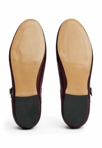 Chaussures en cuir avec une finition bordeaux profond, présentant une tige lisse, des semelles en caoutchouc et un design élégant. Le dessous montre des détails de prise texturés.