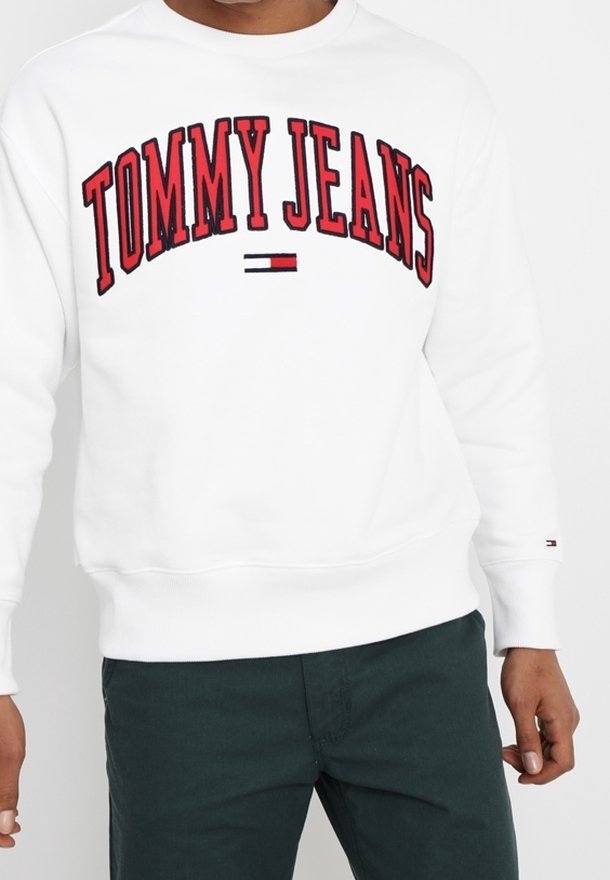 Weißer Pullover mit "TOMMY JEANS" in großen roten Buchstaben, versehen mit einem kleinen Logo-Streifen in Blau, Rot und Weiß am linken Ärmel.