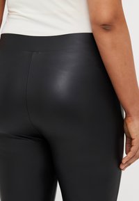 Fekete, műbőr leggings, magas derékkal, sima textúrával és finom varrási részletekkel, bemutatva a hátsó nézetet és a fazont.