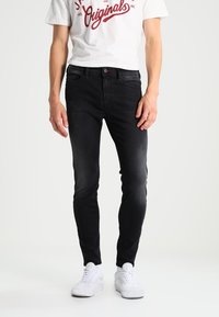 Svarta slim-fit jeans i denim, med en klassisk femficksdesign och subtila sömdetaljer, kombinerade med vita sneakers.