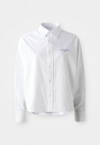 Camisa blanca de botones con rayas verticales en azul claro, un cuello puntiagudo y un pequeño logo azul en el lado izquierdo del pecho. Tejido de algodón, corte relajado.