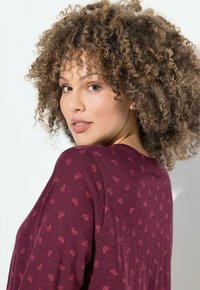 Maglietta a maniche lunghe color bordeaux con un sottile motivo floreale in tonalità più chiare. Tessuto morbido e vestibilità rilassata, con scollatura rotonda.