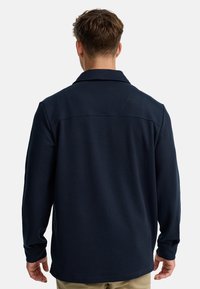 Chemise à manches longues marine avec un design à col, en tissu texturé et à coupe droite. Comprend une couture de yoke au dos pour plus de structure.