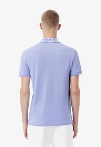 Lichtpaarse polo met een witte geborduurde kraag en korte mouwen, gemaakt van een gladde, ademende stof.