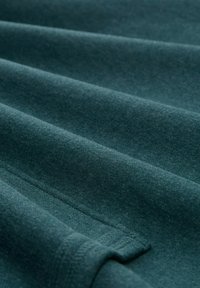 Tessuto verde scuro con una texture liscia, che mostra strati piegati e dettagli di cucitura sottili, con una finitura opaca.