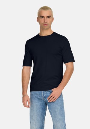 T-shirt blu navy a maniche corte, realizzato in morbido cotone, con scollatura a girocollo e vestibilità ampia, abbinato a jeans in denim blu chiaro.