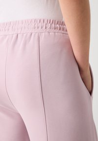 Light pink joggers with an elastic waistband, side pockets, and smooth texture, featuring subtle stitching details along the sides.