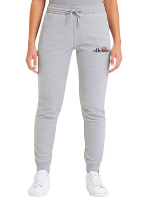 Pantalon de survêtement gris avec une taille élastique, un cordon de serrage et des poches latérales. Il présente un petit logo sur le côté gauche. Associé à des baskets blanches.