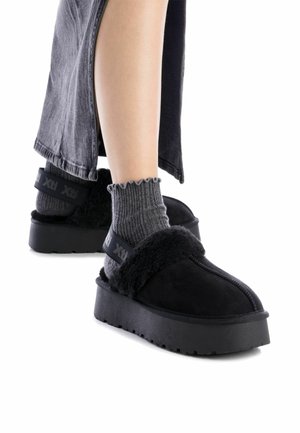 Scarpe con plateau nere con una morbida fascia in pelliccia, abbinate a calze grigie a coste con bordo a onde; le scarpe hanno una suola testurizzata.