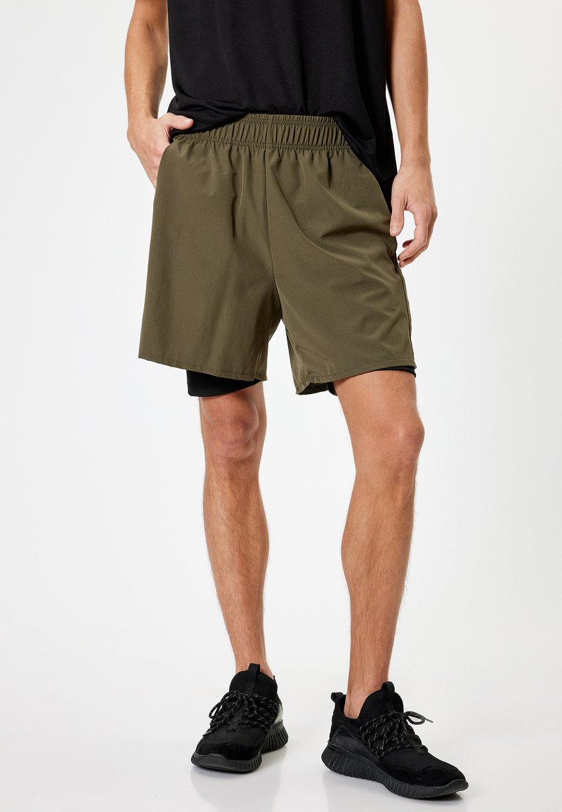 Shorts deportivos de color verde oliva con una cinturilla elástica, textura suave y un ajuste holgado, combinados con zapatillas negras.