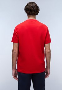 Rød bomulds T-shirt med korte ærmer og rund hals, vist fra ryggen. Har en glat overflade og et mærke på den nederste venstre side.