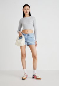 Un haut court gris à manches longues, un short en denim bleu clair, un sac à main matelassé blanc et des chaussures de sport multicolores avec des chaussettes blanches.