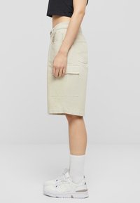 Beige denim midi-skjørt med sidelommer, rett snitt og en sømlinje rett over kneet, kombinert med hvite sneakers og ankelsokker.