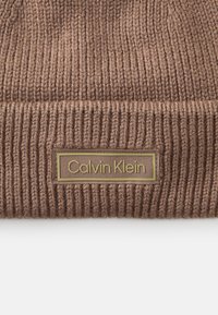 Bračna rebrasta pletena kapa s preklopom, s pravokutnom oznakom Calvin Klein u zlatnoj boji sprijeda. Teksturirani vuneni materijal.