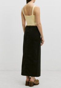 Geribbelde gele crop top met brede banden, gecombineerd met een zwarte denim maxi rok. De rok heeft achterzakken en een rechte silhoeët. Chunky heeled mules.