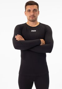 Schwarz langärmliges Sportshirt aus dehnbarem Material mit taillierter Passform. Mit Rundhalsausschnitt und dem "JAKO"-Logo auf der Brust.