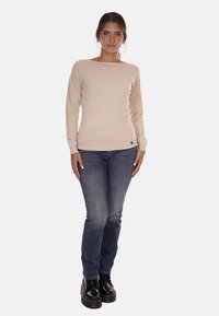 Maglietta a maniche lunghe color beige chiaro in un tessuto morbido, abbinata a jeans blu scuro e stivali neri con lacci. Presenta un collo rotondo e una silhouette aderente.