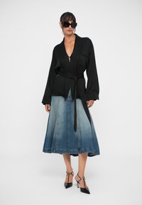 Black wrap blouse with long sleeves, paired with a blue denim skirt featuring a gradient. Black pointed-toe heels complete the look.
