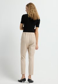 Zwarte ribbel top met korte mouwen gecombineerd met beige tapered broek met een elastische tailleband, gladde textuur en zwarte instapheels.
