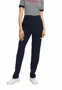 Pantalon bleu marine sur mesure avec une coupe droite, présentant une texture lisse et un devant plat. Associé à des baskets blanches et un haut rayé.