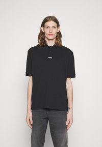 Tricou polo negru cu guler, având o plachetă cu trei butoane și logo-ul alb "HUGO" pe piept. Material din bumbac moale, croială lejeră.