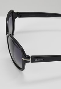 Black sunglasses with a glossy finish, thick frames, gradient lenses, silver accent detailing on the arms, and Polaroid branding.