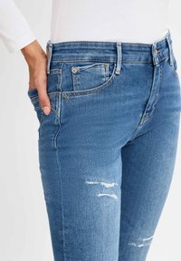 Blaue Jeans aus Denim mit ajustiertem Design, das eine abgewetzte Textur, sichtbare Nähte und Details an den Vorderentaschen aufweist.