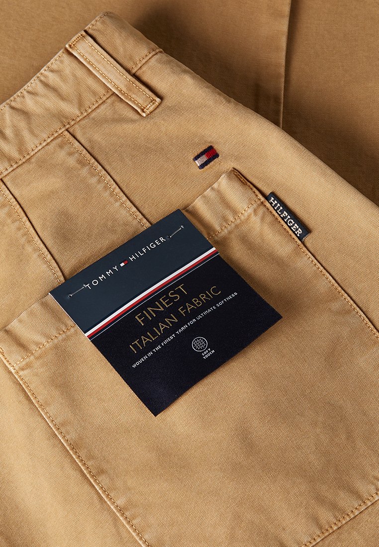 Pantaloni beige realizzati in pregiato tessuto italiano, con un piccolo logo ricamato e un'etichetta con le informazioni sul prodotto.
