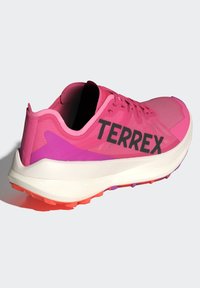 Růžová sportovní bota s pletivovým svrškem, černým logem "TERREX" a barevnou podešví v odstínech oranžové a fialové.