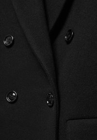 Sort uld blazer med dobbeltbrystet design, glat tekstur og seks blanke sorte knapper. Bemærkelsesværdig fold ved kraven.