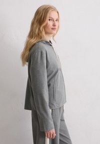 Szara bluza z kapturem o luźnym kroju, wykonana z miękkiego materiału. Szczegóły obejmują centralny zamek błyskawiczny, sznurki do ściągania oraz dwie boczne kieszenie.