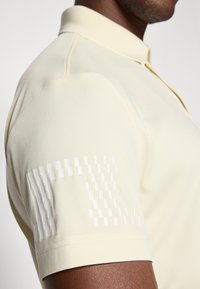 Polo shirt van zacht, lichtgeel materiaal met een gestructureerde kraag. Bevat een textuur met een witte graphic op de linkermouw.