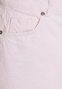 Tissu en denim rose clair en gros plan avec une poche, un bouton-pression argenté et des détails de couture contrastants. Texture douce avec un motif subtil.