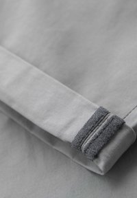 Manche en tissu gris clair avec un détail de manchette texturée gris foncé, pliée sur un fond gris lisse assorti.