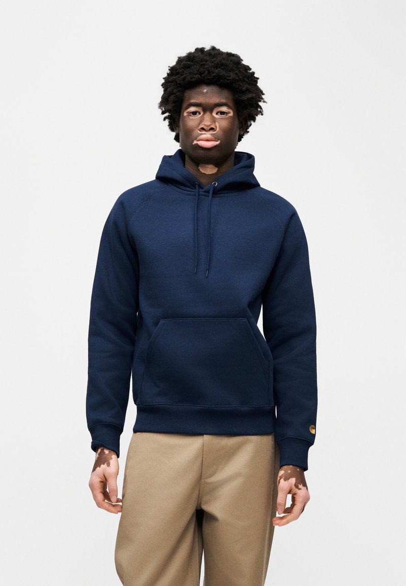 Sweat-shirt à capuche bleu marine en matière douce, avec une poche kangourou à l'avant et des poignets et un ourlet côtelés. Texture lisse, design minimaliste.