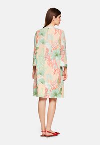 Blumenkleid in zartem Pfirsich, mit grünen und roten Blattmustern. Es hat einen lockeren Schnitt, Dreiviertelärmel und einen mittellangen Saum.