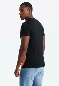 Mustat t-paita lyhyillä hihoilla, joissa on oranssit yksityiskohdat sivuilla. Valmistettu pehmeästä kankaasta, muotoonommeltu malli, jossa on pyöreä kaula-aukko.