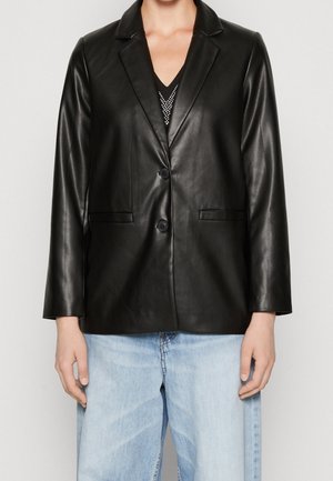 Person iført en sort læderblazer med to knapper over lyseblå jeans og en sort top med sølvnitter.