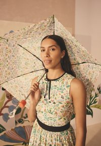 Õiekujundusega vihmavari, millel on roosa ja roheline muster. Kahvel on oranž ning selle tipul on selge ja kaunistustega detail. Modellil on seljas sobiva mustriga kleit.