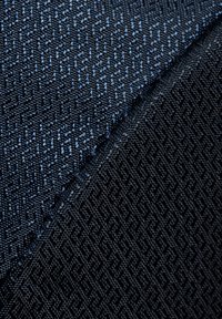 Tessuto testurizzato che mostra due tonalità di blu scuro, caratterizzato da un motivo geometrico con una combinazione di finiture opache e lucide.